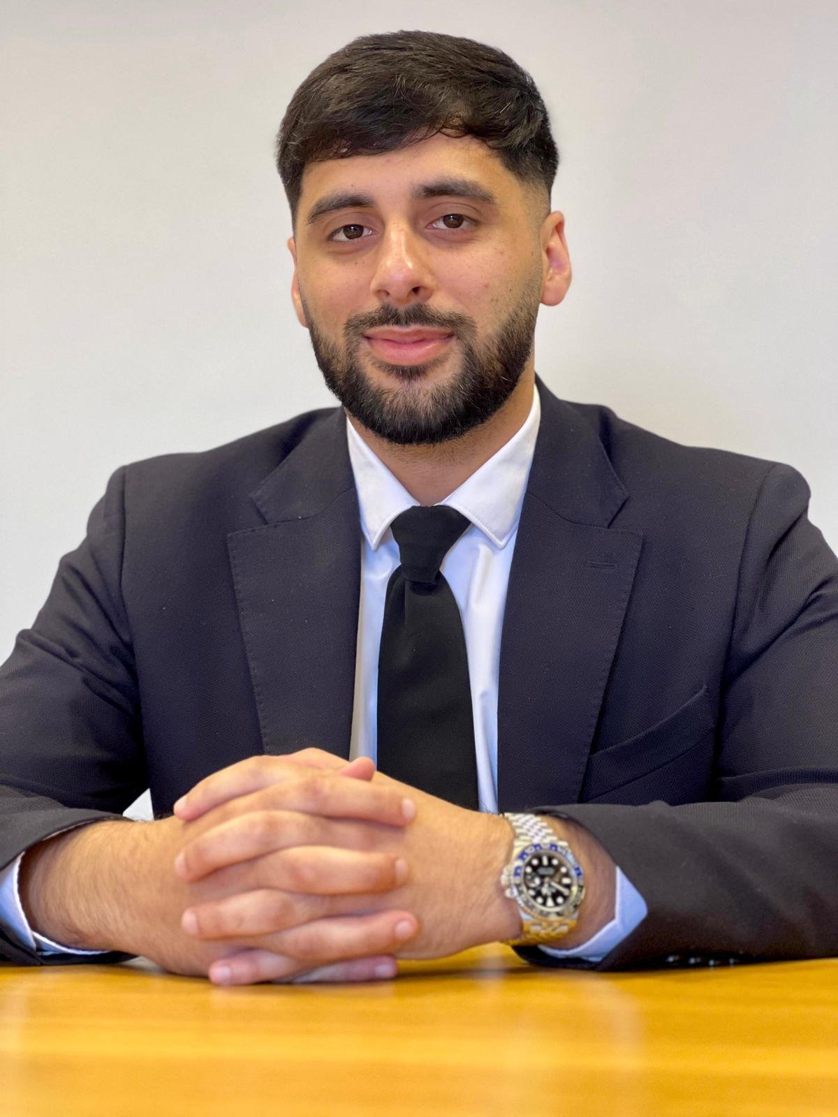 Man in business suit and tie sitting at yellow table, wearing watch, professional portrait against white background
